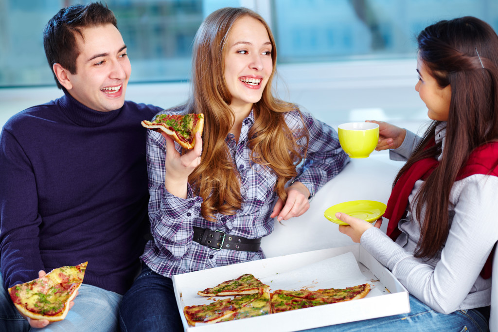 Image of happy teenage friends eating pizza together